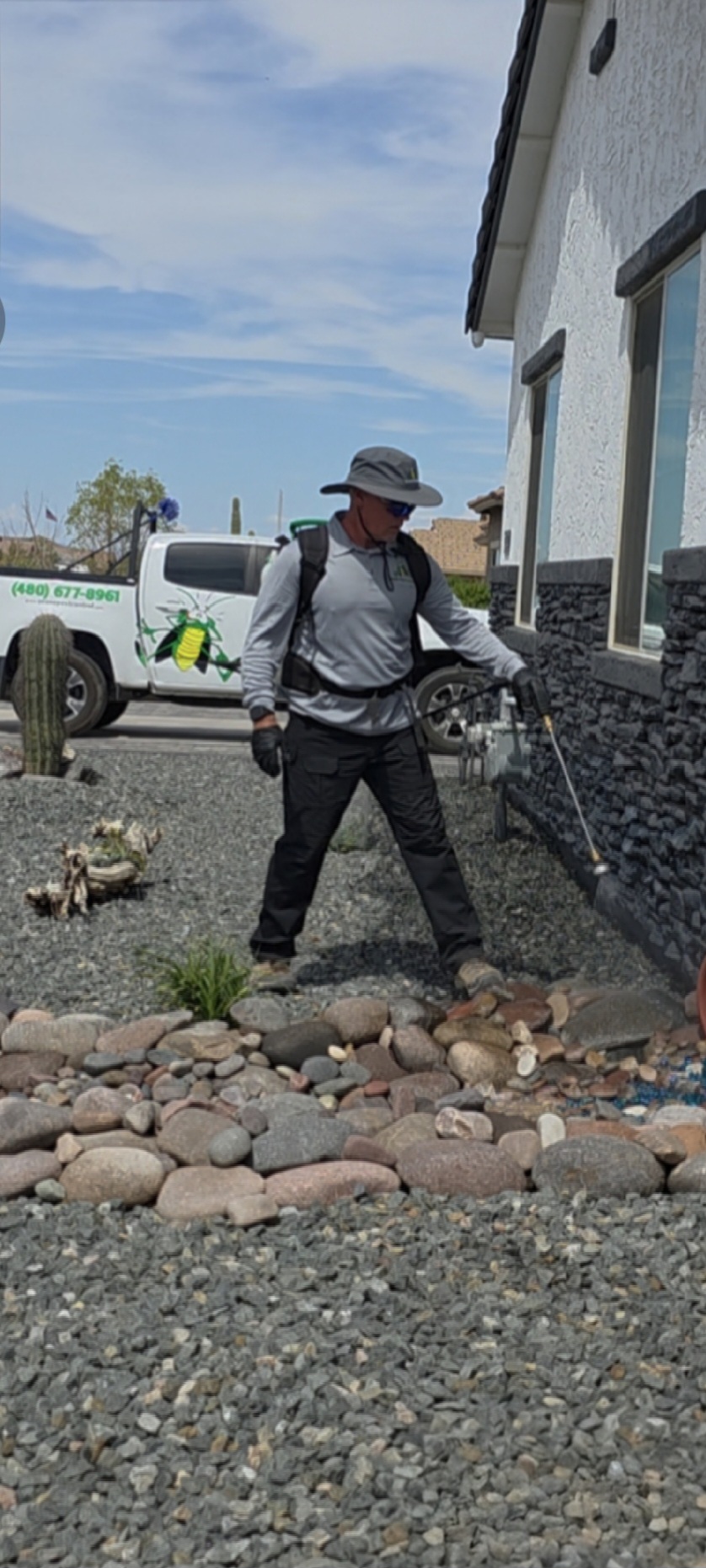 Ozone Pest Control technician spraying the foundation of a home, with a company truck in the background