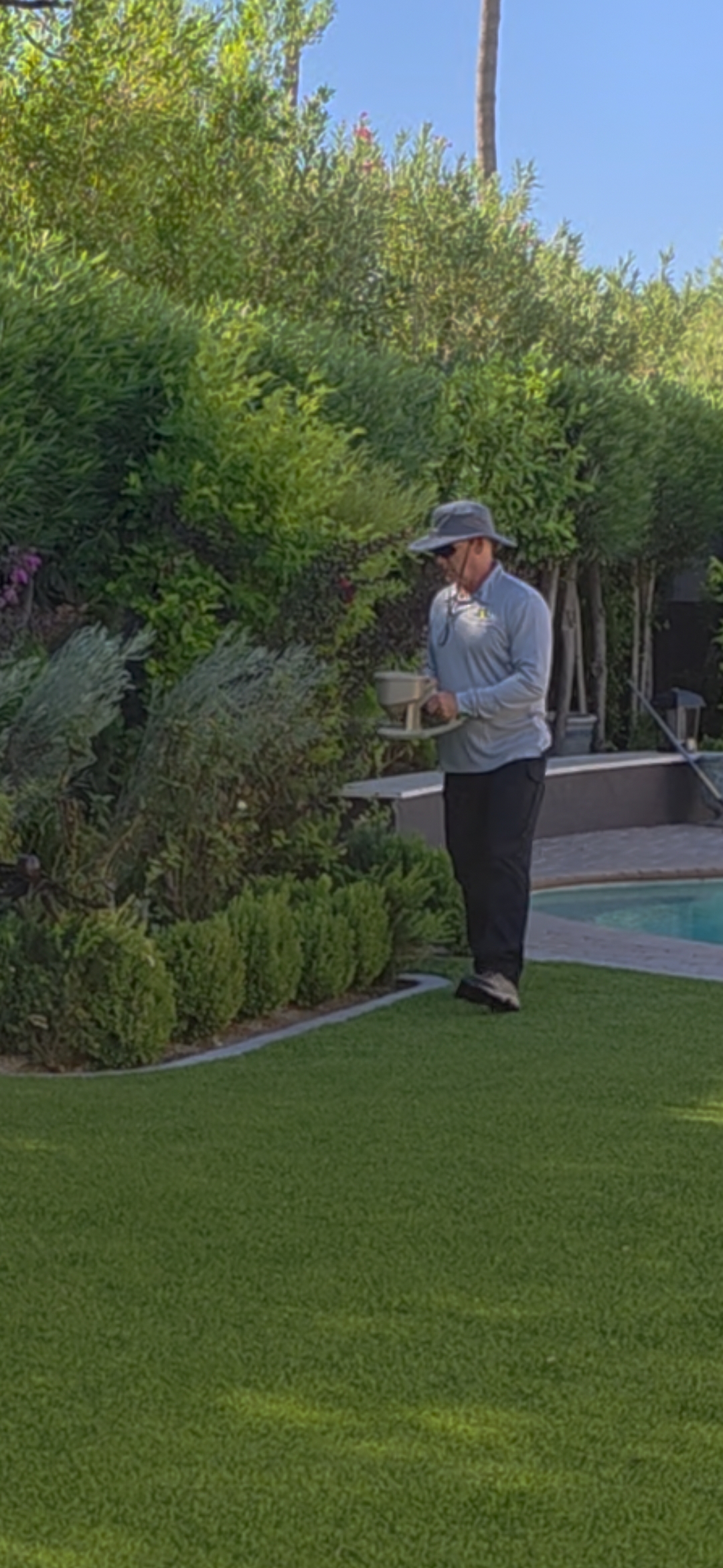 Ozone Pest Control technician applying granular treatment along a hedge next to a pool