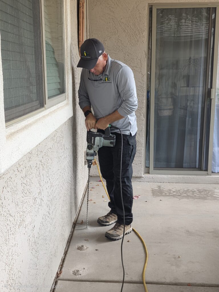 Harry Drilling For Termite Treatment Ozone Pest Control technician drilling into concrete to apply a termite treatment